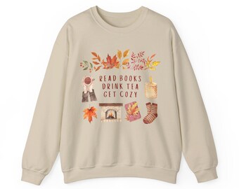 May include: Cream-coloured sweatshirt with a watercolour design of autumn leaves, a cup of tea, a fireplace, a book, a candle, and socks. The text "READ BOOKS DRINK TEA GET COZY" is printed on the front.