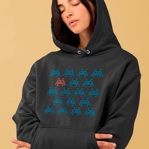 May include: A black hooded sweatshirt with a pixelated design of a group of blue alien spaceships with one red alien spaceship in the center.