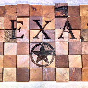 Puede incluir: Una pieza de arte de pared de madera con la palabra "TEXAS" escrita en letras grandes y negras. Una estrella negra de cinco puntas se encuentra en el centro de la pieza.