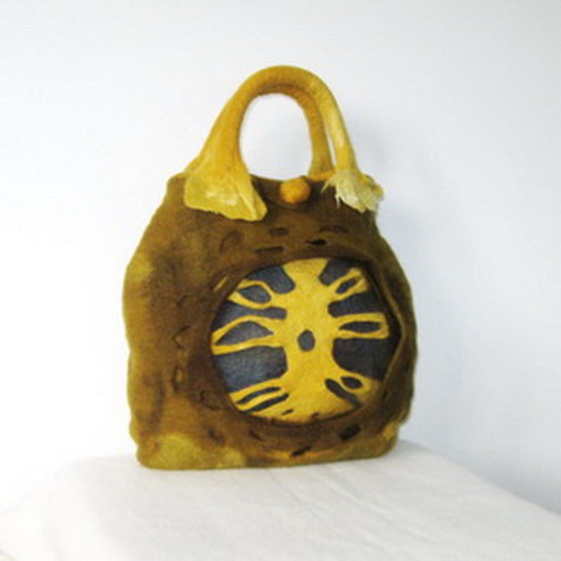 Puede incluir: Un bolso de mano de lana fieltro con un dise&ntilde;o de &aacute;rbol amarillo y marr&oacute;n. El bolso tiene una forma &uacute;nica y org&aacute;nica y un asa larga de color amarillo.