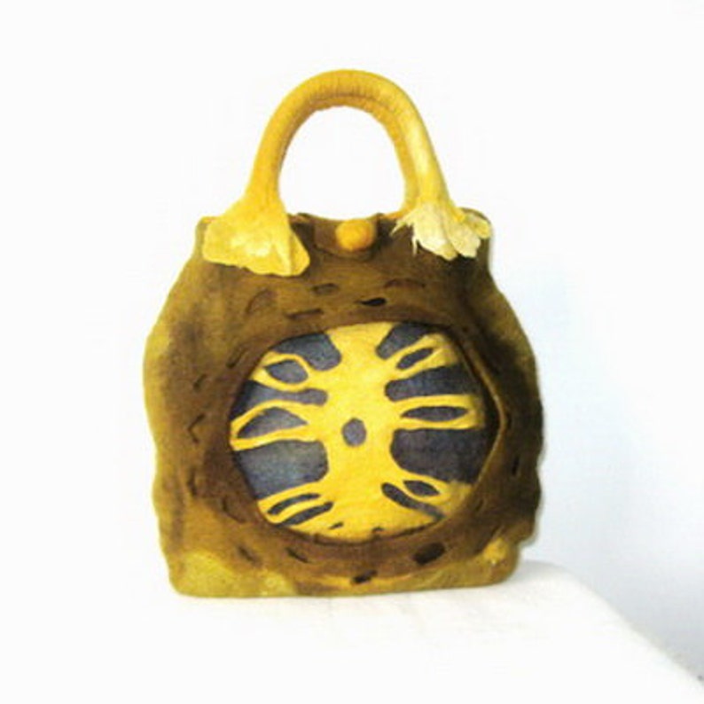 Puede incluir: Un bolso de mano de fieltro marr&oacute;n con un dise&ntilde;o de &aacute;rbol de fieltro amarillo. El bolso tiene un asa de fieltro amarillo.