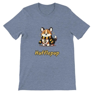 May include: A light blue t-shirt featuring a cartoon corgi wearing a black and yellow scarf and a matching cloak. The text "Hufflepup" is printed in yellow below the corgi illustration.