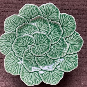 May include: A green ceramic serving dish shaped like a large leaf with a raised design. The dish is made of multiple leaves that are connected together.