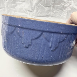 May include: A blue ceramic bowl with a scalloped design around the rim. The bowl has a speckled texture and a light brown rim. The bowl is likely used for food preparation or serving.