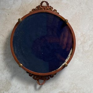 May include: A round, ornate, gold-colored frame with a dark blue velvet backing. The frame has a decorative design with intricate details.