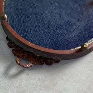 May include: A round, ornate, brass picture frame with a blue velvet backing. The frame has a decorative, scroll-like design around the edge.