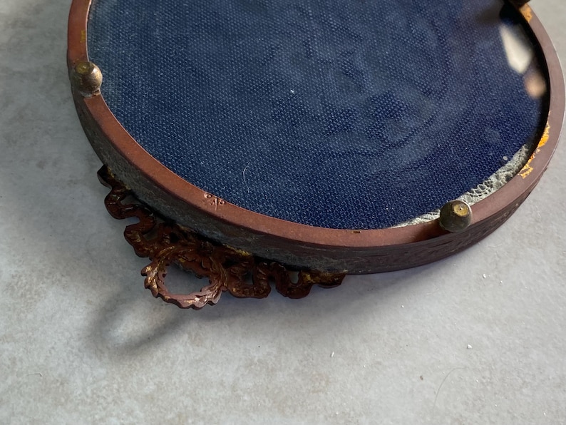 May include: A round, ornate, brass picture frame with a blue velvet backing. The frame has a decorative, scroll-like design around the edge.