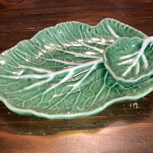 May include: A ceramic serving dish set in the shape of a cabbage leaf, with a matching small leaf-shaped dish. The set is a light green color with white veining details, perfect for serving appetizers or snacks.