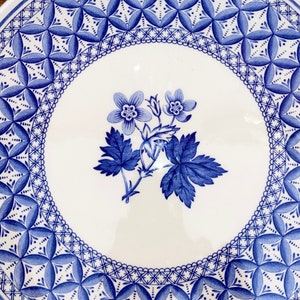 May include: A white ceramic plate with a blue floral design. The plate features a central floral motif and a decorative border with geometric patterns. The blue and white color scheme gives the plate a classic, elegant look.