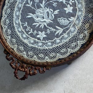 May include: A round, antique, brass tray with a delicate lace design inside. The tray has a decorative, ornate, scroll-like base.