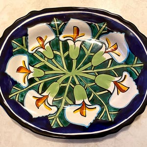 May include: A white ceramic oval serving platter with a blue rim and a floral design. The design features white flowers with orange centers and green leaves on a dark blue background.