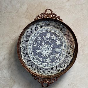 May include: A vintage, round, metal tray with a delicate lace design inside. The tray has a dark brown finish and ornate scrollwork around the edge.
