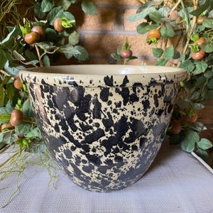 May include: A large, round ceramic bowl with a cream-colored interior and rim. The exterior features a speckled pattern of black spots against a cream background. The bowl is likely for kitchen use.
