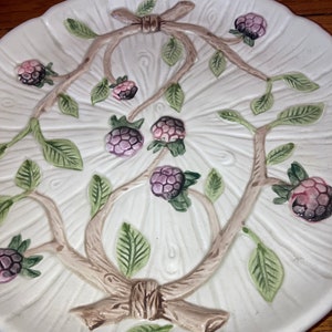 May include: A white ceramic serving plate with a raised design of a tree branch with green leaves and purple berries. The plate has a scalloped edge.