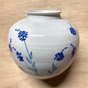 May include: White ceramic vase with a blue floral design. The vase has a round body and a wide mouth.