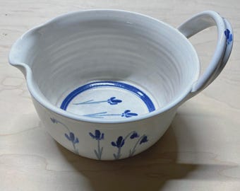 May include: White ceramic mixing bowl with a blue floral design and a handle. The bowl has a spout on one side.