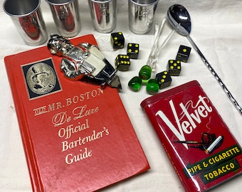 May include: A red book titled "Old Mr. Boston De Luxe Official Bartender's Guide" with a silver bottle opener shaped like a man in a red and white suit. There are four silver shot glasses, a silver spoon, and a red tin with the words "Velvet Pipe & Cigarette Tobacco" on it. There are also several green and yellow dice scattered around.