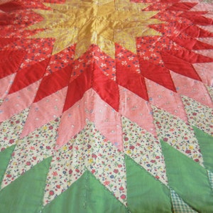 May include: A colorful patchwork quilt with a starburst pattern in shades of red, pink, green, and yellow. The quilt is made of various floral fabrics.