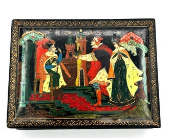 May include: A black wooden box with a gold trim and a painted scene of three people in medieval clothing. The scene is set against a backdrop of a castle and a red carpet.