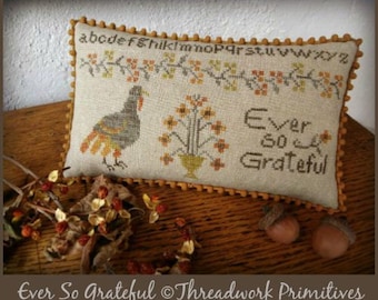 May include: A beige cushion with a brown trim and a cross-stitch design featuring a turkey, flowers, and the text "Ever So Grateful".
