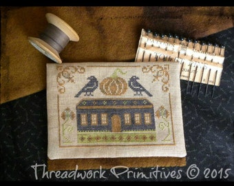 May include: A cross-stitch pattern featuring a small house with a pumpkin on the porch and two black crows perched on the roof. The pattern is framed by a beige fabric with a brown border. The text "Threadwork Primitives © 2015" is printed below the pattern.