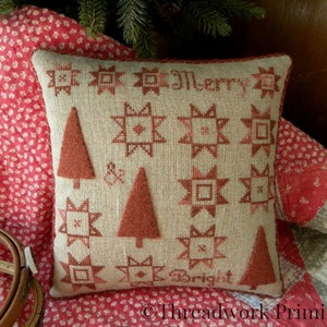 May include: A beige pillow with red embroidered stars and trees, and the text "Merry & Bright".