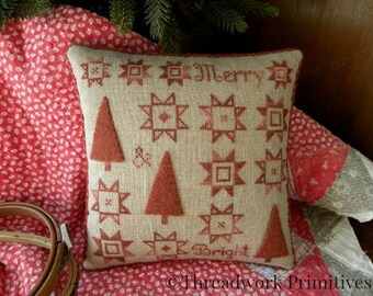 May include: A beige pillow with red embroidered stars and trees, and the text "Merry & Bright".