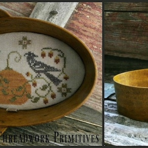 May include: A wooden oval-shaped basket with a handle. The basket is filled with a cross-stitch piece depicting two black birds perched on branches with a pumpkin in the center. The text "THREADWORK PRIMITIVES" is visible at the bottom of the image.