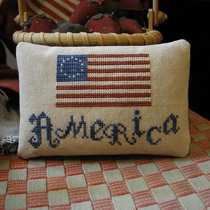May include: A white pillow with a red, white, and blue embroidered American flag and the word "America" in blue embroidery.