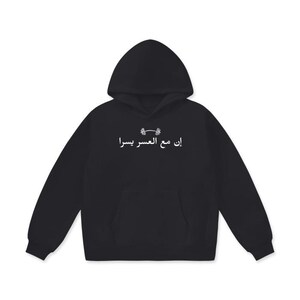 May include: Black hoodie with a hood and a front pocket. The hoodie features white Arabic text and a small graphic above the text. The hoodie is made of a soft material.