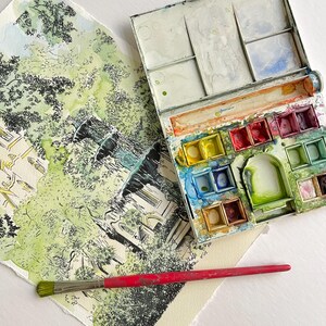 May include: A watercolor painting of a fountain in a park, with a paintbrush and a watercolor palette with various colors of paint.