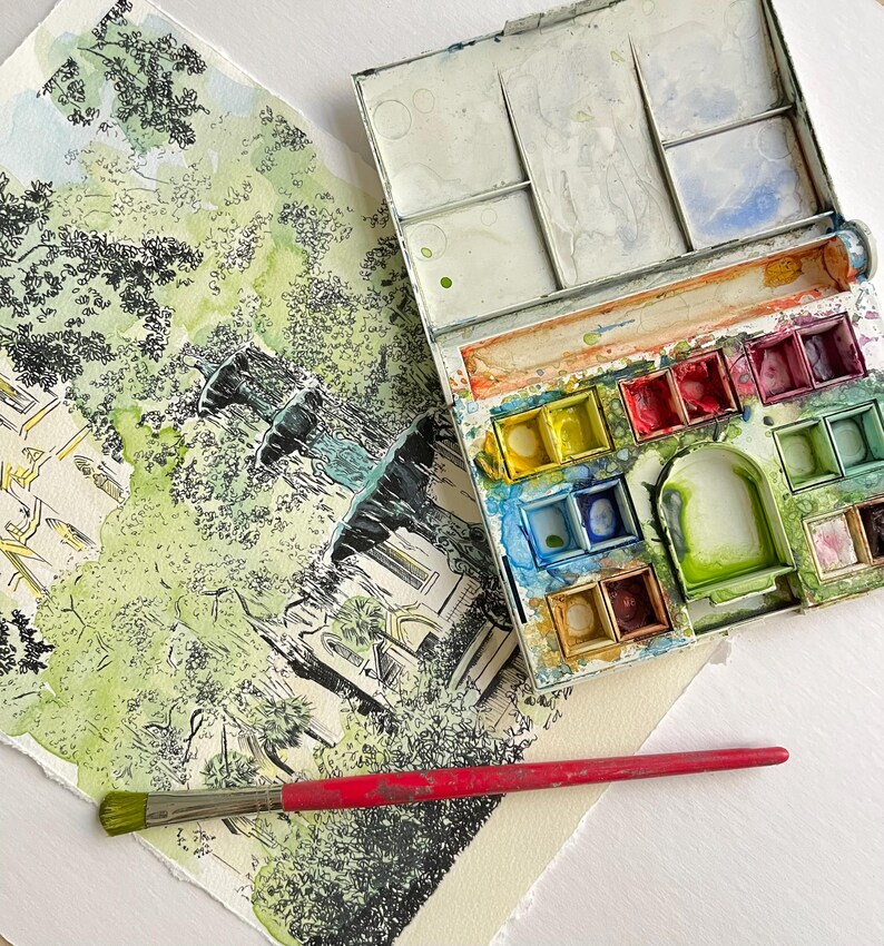 May include: A watercolor painting of a fountain in a park, with a paintbrush and a watercolor palette with various colors of paint.