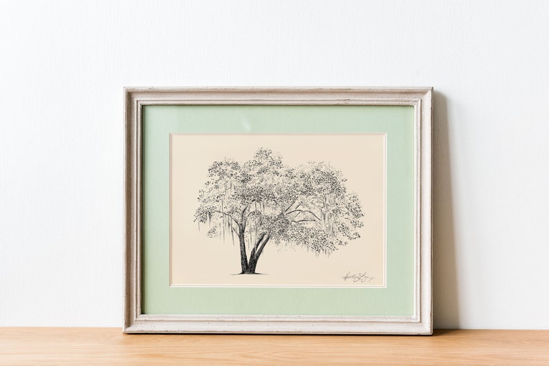 May include: A framed black and white pen and ink drawing of a tree with long branches and hanging vines. The drawing is on a cream background with a light green mat and a white frame.