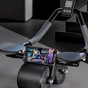 Puede incluir: Una máquina de ejercicio negra y gris con dos ruedas y una pantalla digital de temporizador. La máquina tiene dos reposabrazos y un soporte para teléfono. El soporte para teléfono muestra un video de una persona haciendo ejercicio.