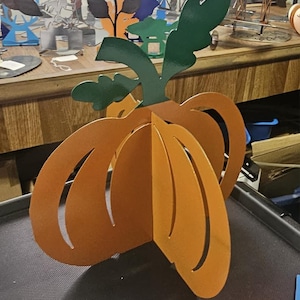 Puede incluir: Decoración de calabaza de metal naranja tridimensional con hojas y tallo verdes. La calabaza tiene cortes curvos y está diseñada para mantenerse de pie. Una decoración festiva de otoño o Halloween.