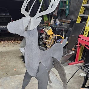 May include: A large, metal deer sculpture with a gray finish. The deer has a stylized design with large antlers and a slender body. The sculpture is made of welded metal sheets and stands on a metal surface.