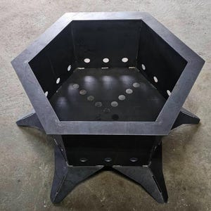 Puede incluir: Un brasero negro y geométrico con una parte superior hexagonal y una base robusta en forma de estrella. El brasero tiene múltiples orificios de ventilación circulares y está hecho de metal oscuro. El diseño es moderno y adecuado para uso en exteriores.