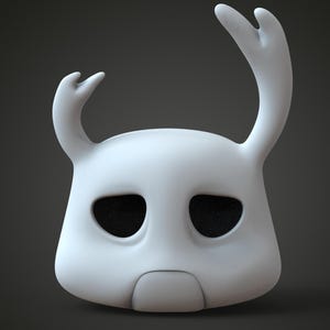 Puede incluir: Una máscara blanca estilizada con dos cuernos curvos y grandes aberturas ovaladas para los ojos. La máscara tiene una forma suave y redondeada y una pequeña abertura rectangular para la boca. Las aberturas de los ojos son negras.