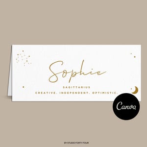May include: A white place card with gold lettering and a constellation design. The name "Sophie" is written in cursive. The text "Sagittarius, Creative, Independent, Optimistic" is also included. A crescent moon icon is in the bottom right corner.