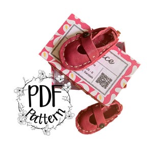 May include: A pair of small, red leather sandals with button closures, resting on a pink patterned box. The sandals are hand-stitched with white thread. The box has a label with text and a QR code. The image also includes the text "PDF Pattern".