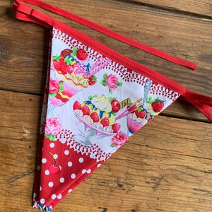 May include: A red and white fabric bunting with a pattern of ice cream sundaes and cherries. The bunting has a red trim and white polka dots.