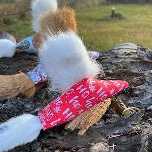 May include: Cat toys with fluffy white, brown, and orange fur tails. The toys have fabric bases with festive patterns and the words "HO HO HO" printed on a red background. The toys are arranged on a piece of wood.