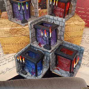 Peut inclure: Mini-dioramas fantastiques avec des murs en pierre, des tissus drapés et des candélabres avec des bougies colorées. Les scènes se déroulent dans de petites pièces cubiques. Une plume avec des engrenages décoratifs est également visible.