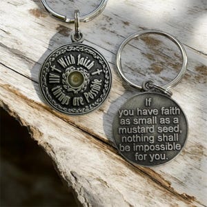 Puede incluir: Un llavero de plata con un dije redondo que dice "Con fe todo es posible." La parte posterior del dije tiene una cita de la Biblia: "Si tienes fe tan pequeña como una semilla de mostaza, nada te será imposible."