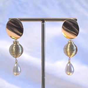 May include: Gold tone drop earrings with a round, textured ball and a pearlescent drop.