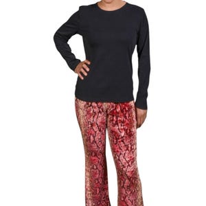 May include: A woman wearing a black long-sleeved shirt and red and gold snake print pants.