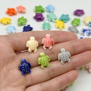 May include: A collection of small, turtle-shaped beads in various colours including blue, green, pink, yellow, orange, and white. Each bead features a detailed shell pattern on the back and a smooth, glossy finish, suitable for jewellery making projects.