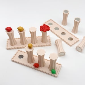 Op de afbeelding: Een verzameling beige, rechthoekige basissen met geschulpte randen en gecanneleerde cilindrische zuilen. Sommige zuilen hebben kleine, kleurrijke fruitvormige toppers in rood, geel en groen, of een rode bloem. Verschillende onderdelen bevatten ronde magneten.