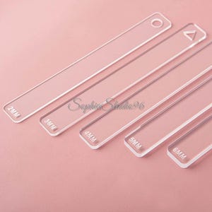 May include: A set of five clear acrylic rectangular guides with rounded corners, each labeled with thickness measurements of 2mm, 3mm, 4mm, 5mm, and 6mm. The longest guide features a circular hole at one end, while another includes a triangular cutout.