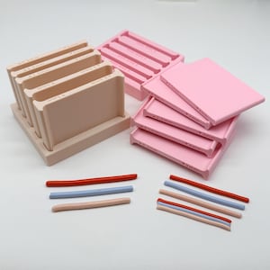 Op de afbeelding: Een set beige en roze plastic klei-extrusiegereedschappen met rechthoekige basissen en verticale sleuven. Elke sleuf is gelabeld met afmetingen variërend van 1mm tot 5mm. Verschillende dunne, cilindrische kleistrips in rood, blauw en beige liggen eronder.